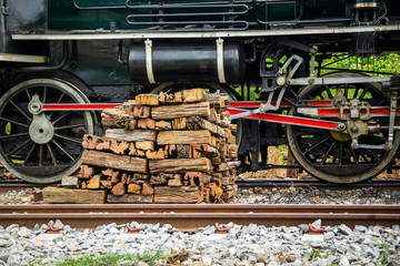 Fototapeta na wymiar Focus detail Wheel Mechanism of the train old Steam locomotive of Japanese World War II at Thailand. and pile wood prepared for firewood.