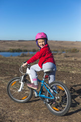 Little girl with a bicycle in the field at autumn time
