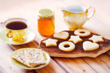 Beautiful set of homemade cookies stars and hearts on the brown decorative board, vintage cup of tea and honey. Sunny morning. Food, break, cooking, lifestyle concept. Top view. Close up.