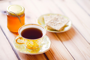 Vintage cup of tea with natural sweets and jar of honey on the wooden background. Sunny morning.  