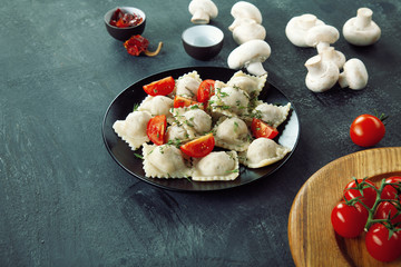 Close up view on fresh ravioli with slice cherry tomato, mushroom and herbs on black plate and dark background. Free copy space for text.  Restaurant, food menu, recipe, cafe concept. Italian cuisine.