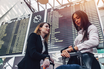 Two female tourists standing near flight information display in international airport