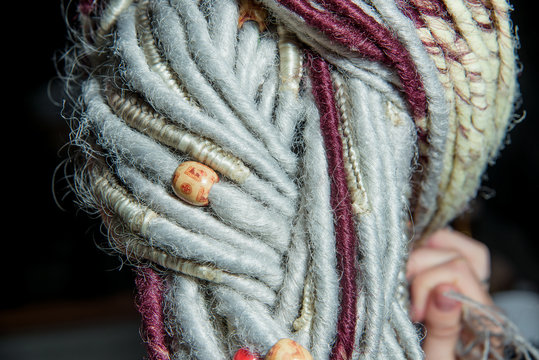 Light colored dreadlocks on the hair. Hair accessories. Dreadlocks braided in pigtails. Pierced ear. Girl. Wooden beads on dreadlocks. Dred texture.