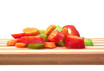 Red and green sliced peppers on wooden chopping board on white background.