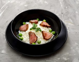Rice with meat pieces, basil and green peas in a plate on a gray background   