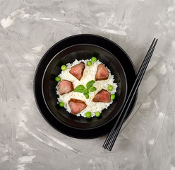 Rice with meat pieces, basil and green peas in a plate on a gray background.  Top view.