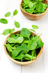 Fresh green spinach leaves on wooden bowl on white wooden rustic background top view copy space. Baby young spinach leaves, Ingredient for salad, healthy food, diet. Nutrition concept.