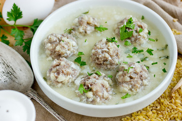 Armenian white sour soup on chicken broth with meatballs, bulgur and green parsley