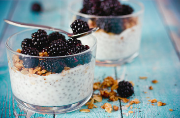 Chia pudding with granola and fresh blackberry in glass on blue wooden background, healthy food idea