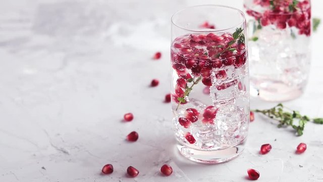 Festive drinks, gin and tonic pomegranate cocktail or detox water with ice. Selective focus, copy space for text, light gray concrete table surface.