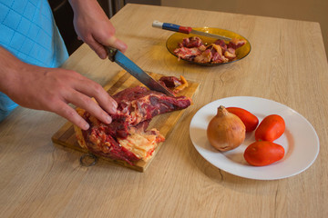 a man in a kitchen apron, meat on a board and a wooden table