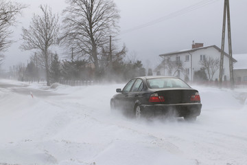 A car sneaks through drifts on a dangerous road covered with snow. Private transport is struggling with the winter elements. Difficulties in traffic during a snowstorm.The consequences of cold weather