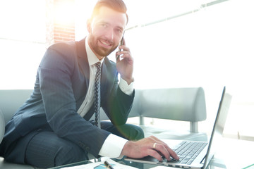 Businessman talking on smartphone and typing text on laptop