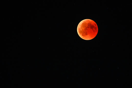 Astronomical background. Closeup of full red moon over dark black sky. The total phase of lunar eclipse on July 27, 2018. Moon turning red cause of closer Mars planet to the moon's surface. - Powered by Adobe