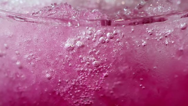 Abstract beauty in drink details. Extreme close-up of iced red soda drink in glass. Crushed ice and fizzy bubbles create beautiful texture patterns.