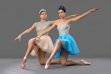 Fototapeta na wymiar Adorable ballet dancers sitting on knees and raising hand up