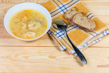 Bowl of clear salmon soup, spoon, bread on rustic table