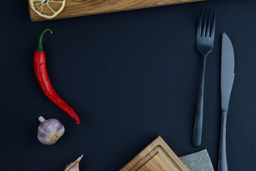Wooden board near pepper, cutlery and garlic
