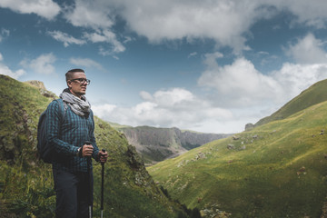 Traveler Man With Backpack And Trekking Poles Resting And Looking At The Mountains In Summer Outdoor
