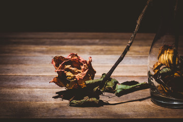 close-up of withered dry rose and leaves falling from vase on wooden table