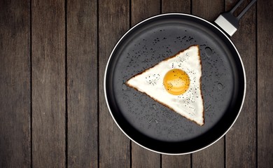 Fried egg with triangle shape on frying pan on wooden background