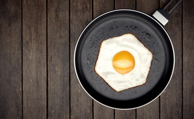 Fried egg with hexagon shape on frying pan on wooden background