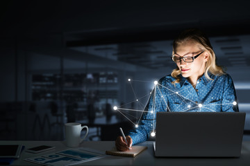 Attractive blonde wearing glasses in dark office using laptop. Mixed media