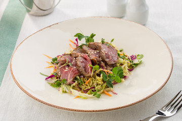 meat salad with roast beef, greens and sesame seeds asian style served on the table