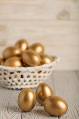 Happy easter! Easter eggs of golden color on a light wooden background.