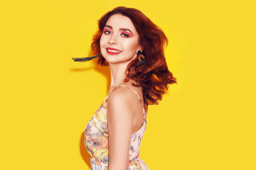 Fashion girl in dress on yellow background dancing. Pretty girl with long cerly flying hair and pink make up. Girl with long green earrings. Portrait with smile. Blithesome ginger lady having fun.