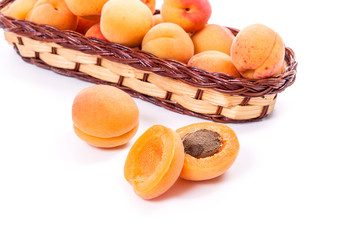 Several of harvested apricots in basket with whole and halved apricots on white background..