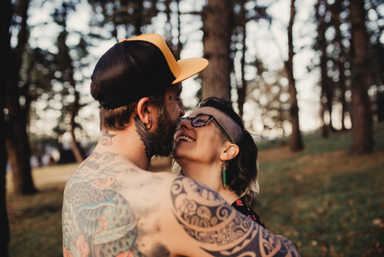 Young guy in tattoos hugging lady in forest