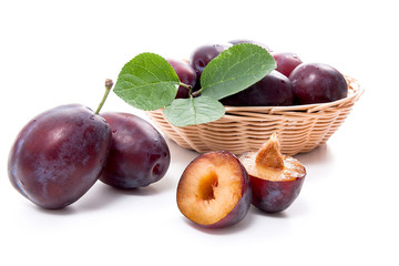 Yellow wooden basket with ripe plums, whole and half ripe plums isolated on a white background..