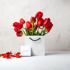 White Gift bag, small white gift box and bouquet of red tulips on a light stone background. Concept Offers an engagement or marriage