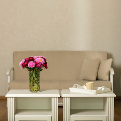 Beige sofa with pillows in the living room and vase with Flowers (Michaelmas daisy, asters).