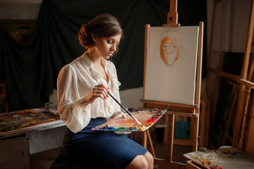 Female painter holds color palette and brush