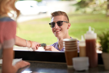 street sale, payment and people concept - happy young man paying money at food truck