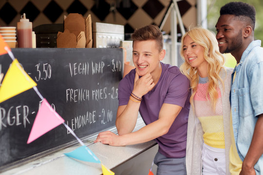 street sale and people concept - happy customers or friends looking at billboard at food truck