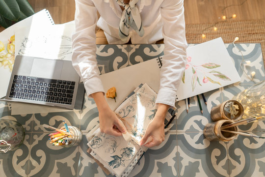 Woman at table with laptop, brushes, materials and papers