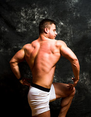 Fototapeta na wymiar Bodybuilder flexing muscles against dark background