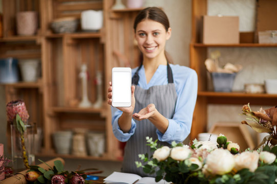 Waist up portrait of smiling female florist holding smartphone with blank screen presenting mobile app, copy space