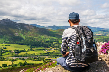 Tourist carrying a backpack, resting after a hike and enjoying the beautiful view of the green...