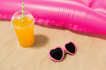 vacation and summer holidays concept - pink sunglasses, orange juice and swimming mattress on beach sand