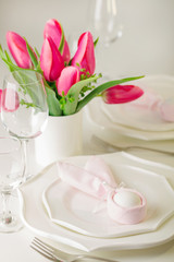 Happy easter. Decor and table setting of the Easter table is a vase with pink tulips and white dishes.