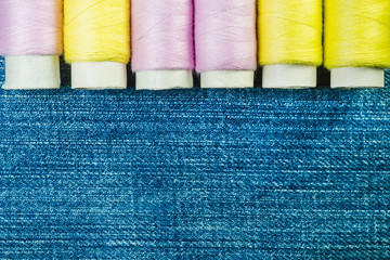 Spools of pink and yellow sewing thread on blue denim with copy space