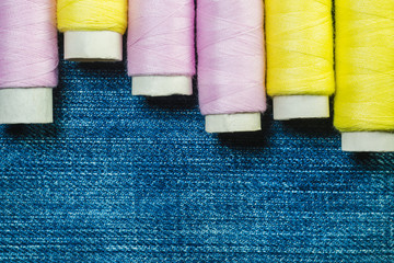 Spools of pink and yellow sewing thread on blue denim with copy space