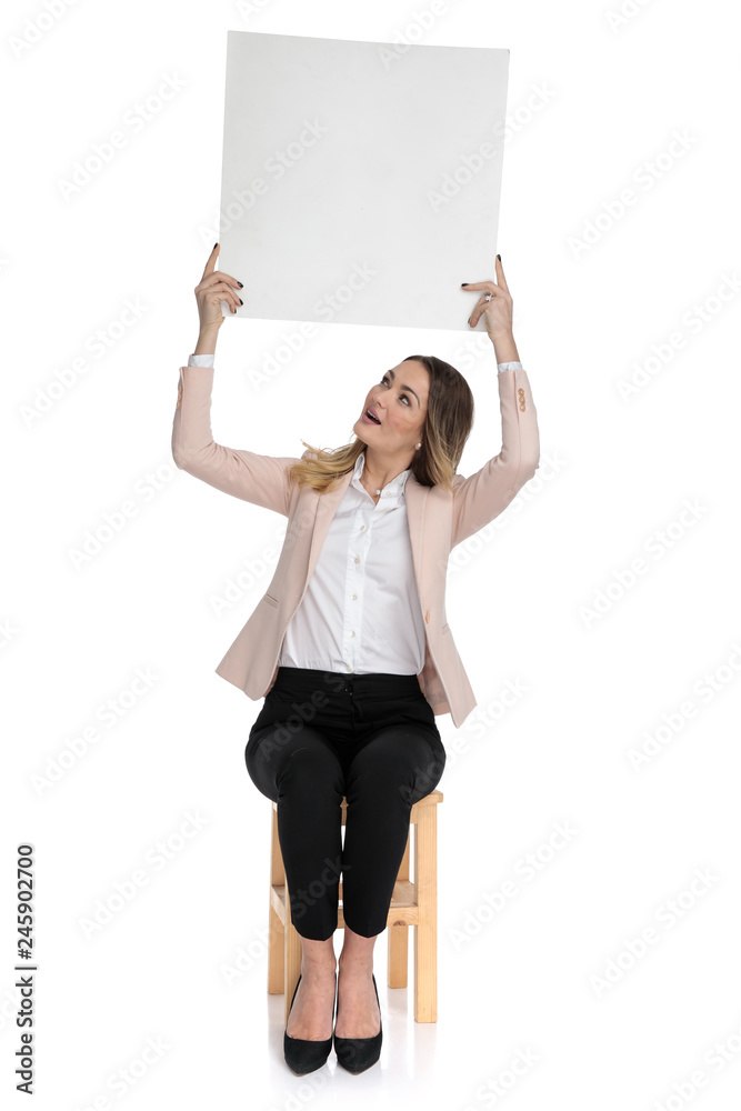 Sticker seated businesswoman in pink suit holds board and looks up