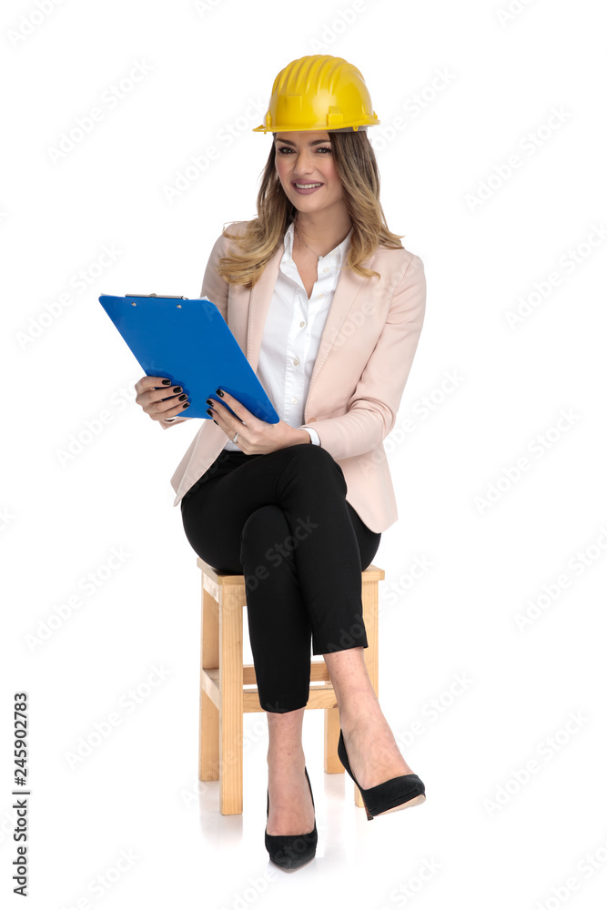 Sticker young businesswoman wearing engineer hat holds blue clipboard