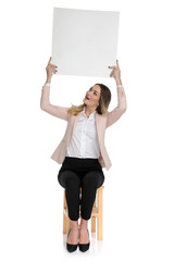 seated businesswoman in pink suit holds board and looks up