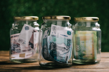 close-up view of glass jars with russian rubles banknotes on wooden table